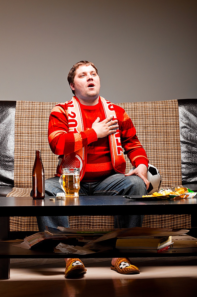 soccer supporter is sitting on sofa in red jersey