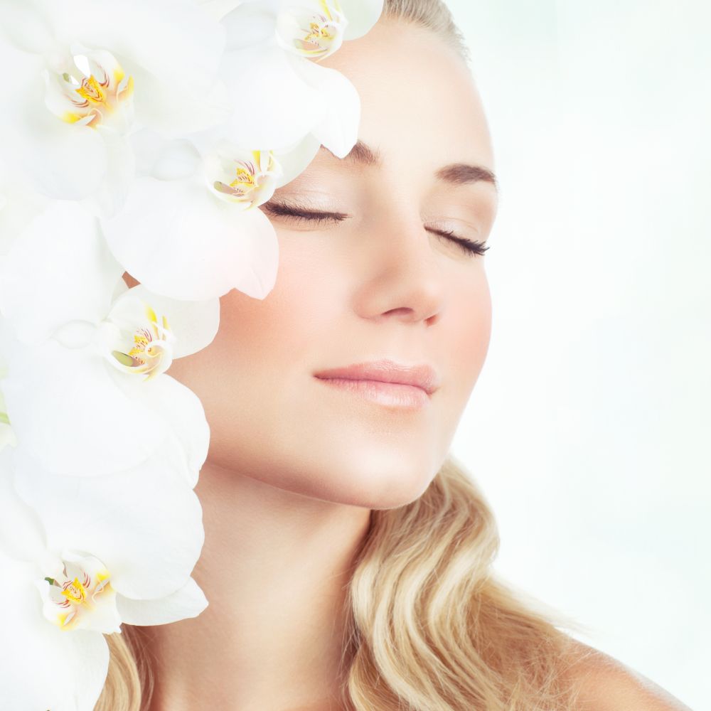 Closeup portrait of a gentle female with closed eyes, many white tender orchid flowers near face, healthy skin, beauty salon