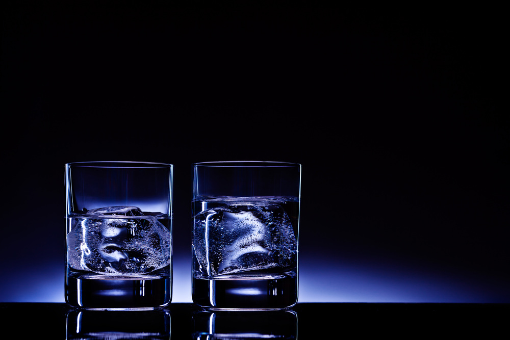 Two glasses of vodka with ice cubes against the background of deep blue glow.