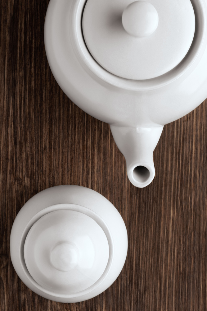 An image of white china tea pot and sugar bowl on wooden table.
