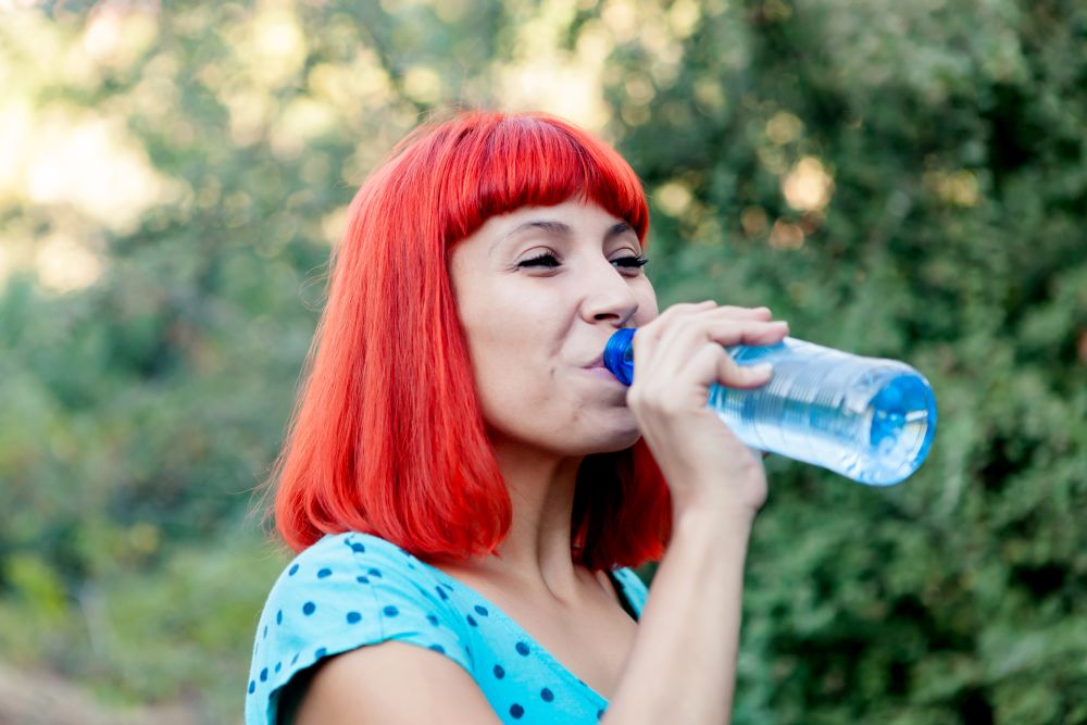 Attractive redhead girl drinking water in a park