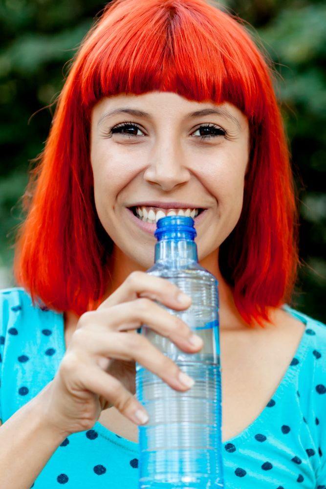 Attractive redhead girl drinking water in a park