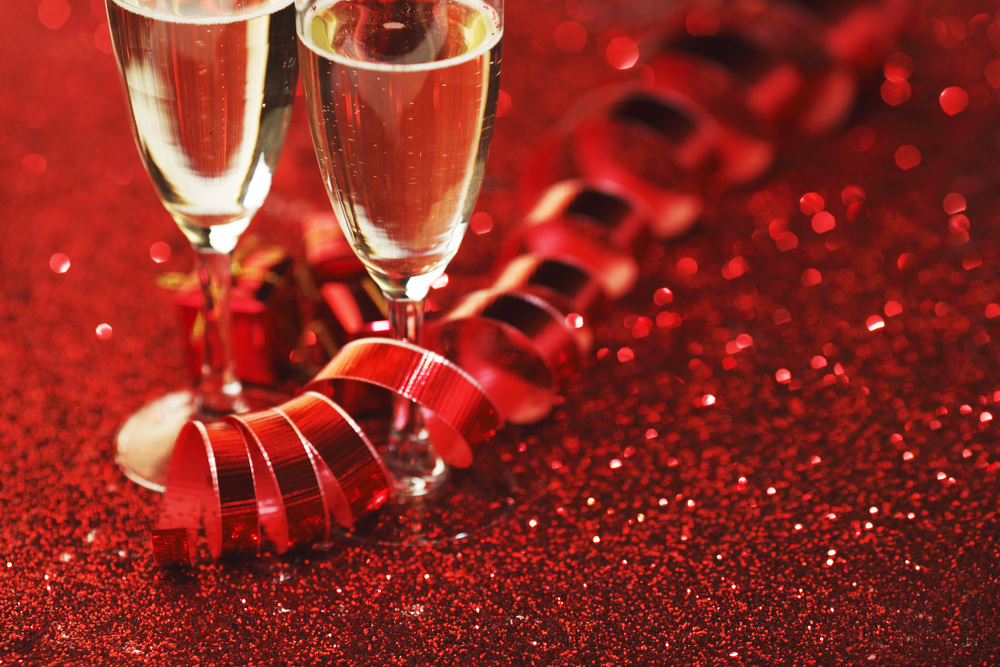 Glasses with Champagne and gifts on red glitters background. Champagne on glitters