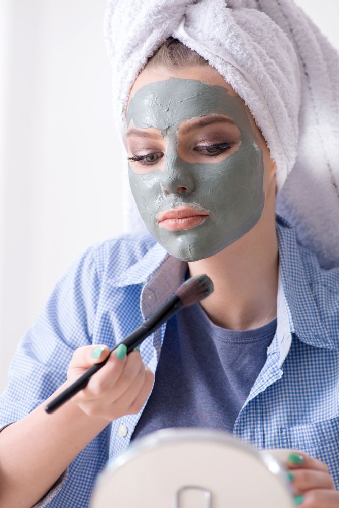 Woman applying clay mask with brush at home