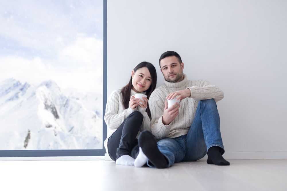 happy young multiethnic couple enjoying morning coffee by the window on cold winter day at home