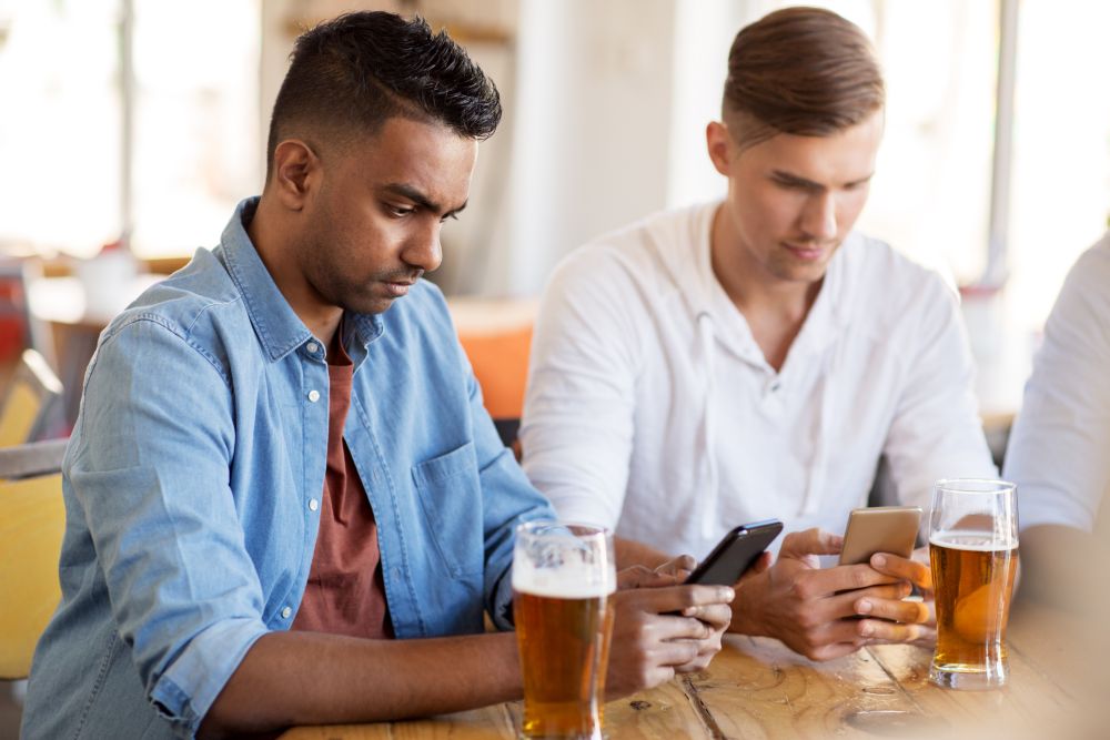 people and technology concept - male friends with smartphone drinking beer at bar or pub. male friends with smartphone drinking beer at bar