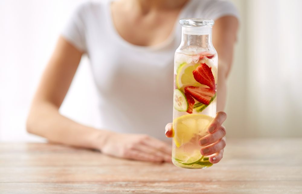 healthy eating, detox and people concept - close up of woman with fruit water in glass bottle at home. close up of woman with fruit water in glass bottle