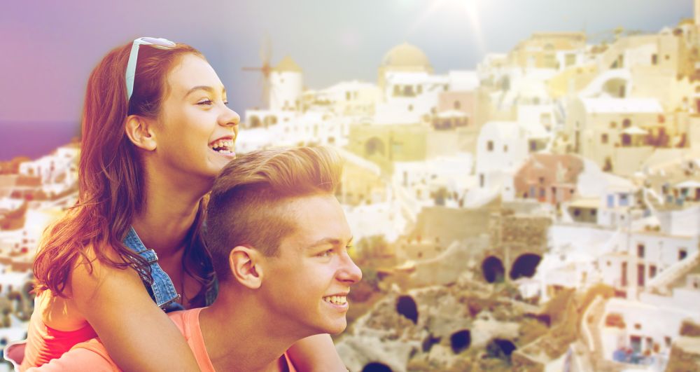 travel, tourism and people concept - happy smiling teenage couple having fun over oia town on santorini island background. happy teenage couple having fun on santorini