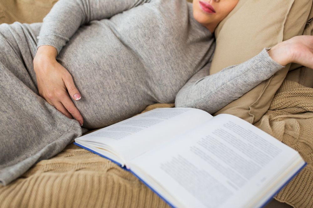 pregnancy, people and motherhood concept - close up of pregnant woman with book sleeping at home. close up of pregnant woman with book sleeping