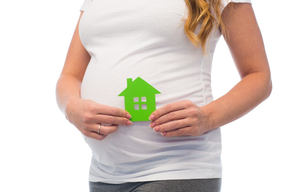 pregnancy, ecology, people and housing concept - close up of pregnant woman with green house icon. close up of pregnant woman with green house icon
