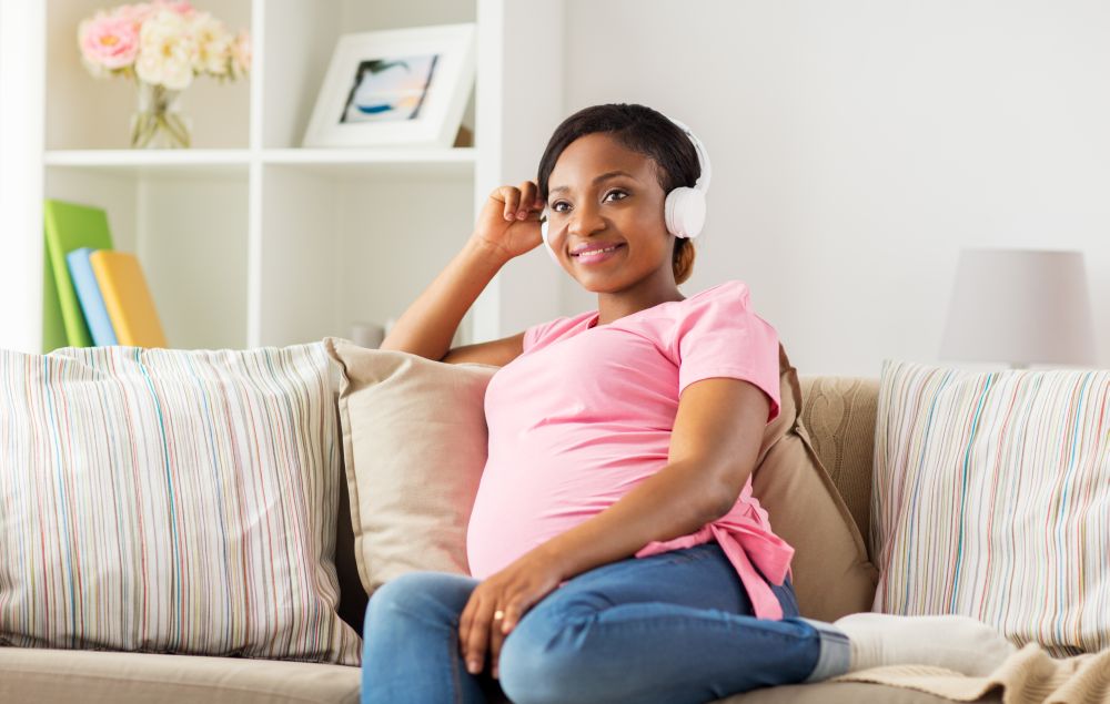 pregnancy, technology and people concept - happy pregnant african american woman with headphones listening to music at home. pregnant woman in headphones at home