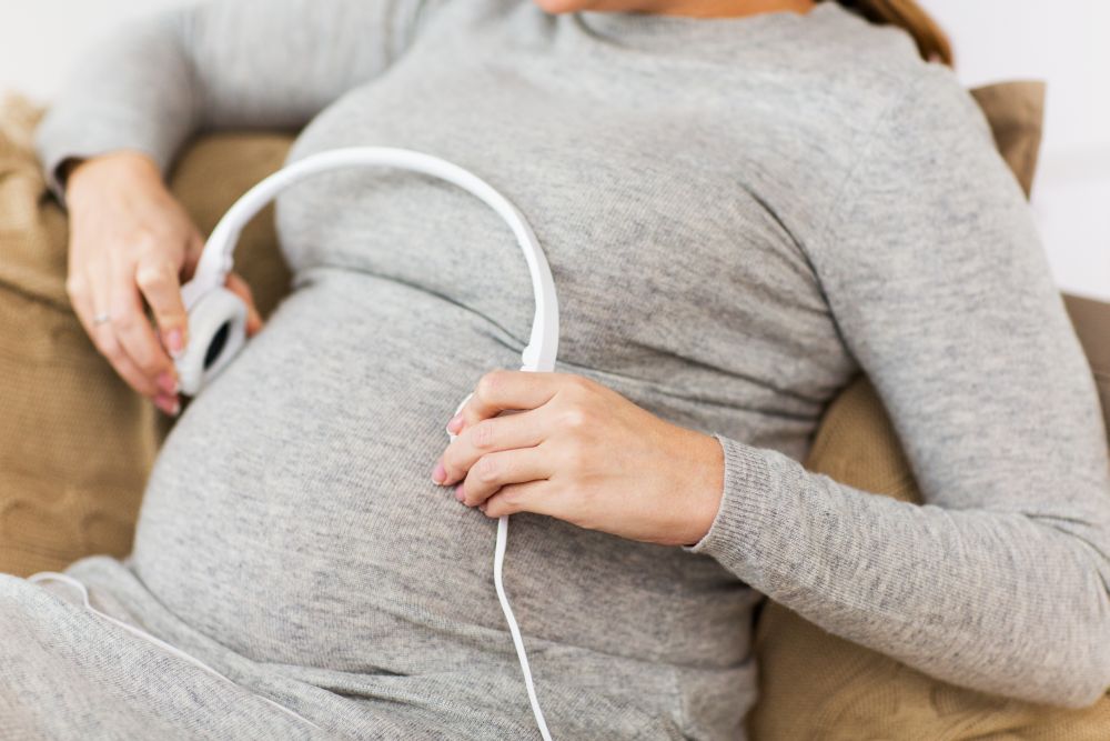 pregnancy, technology and people concept - close up of pregnant woman with headphones on her belly at home. pregnant woman with headphones listening to music