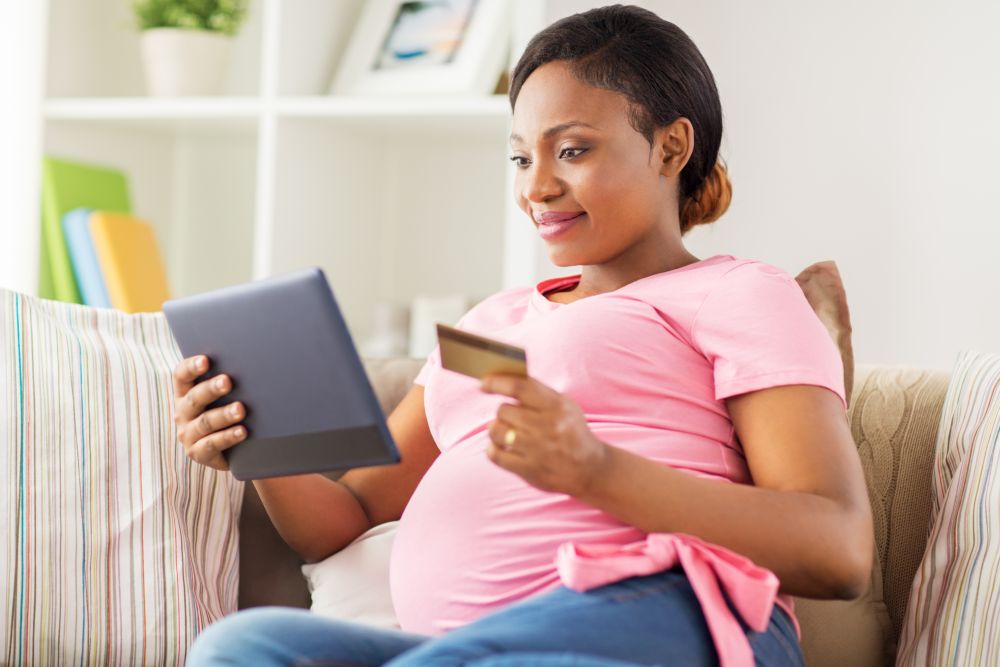pregnancy, online shopping, technology and people concept - happy pregnant african american woman with tablet pc computer and credit card at home. pregnant woman with tablet pc and credit card