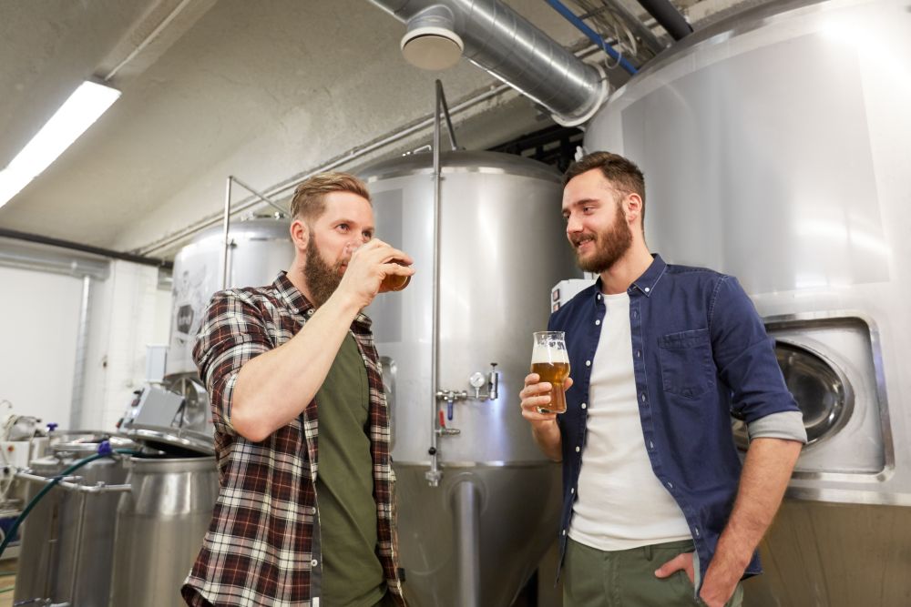 production, manufacture, business and people concept - men testing and drinking non-alcoholic or craft beer at brewery. men testing non-alcoholic craft beer at brewery