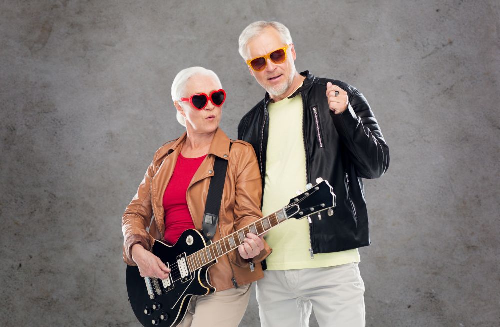 music, age and people concept - happy senior couple in sunglasses with electric guitar over gray concrete background. senior couple in sunglasses with electric guitar