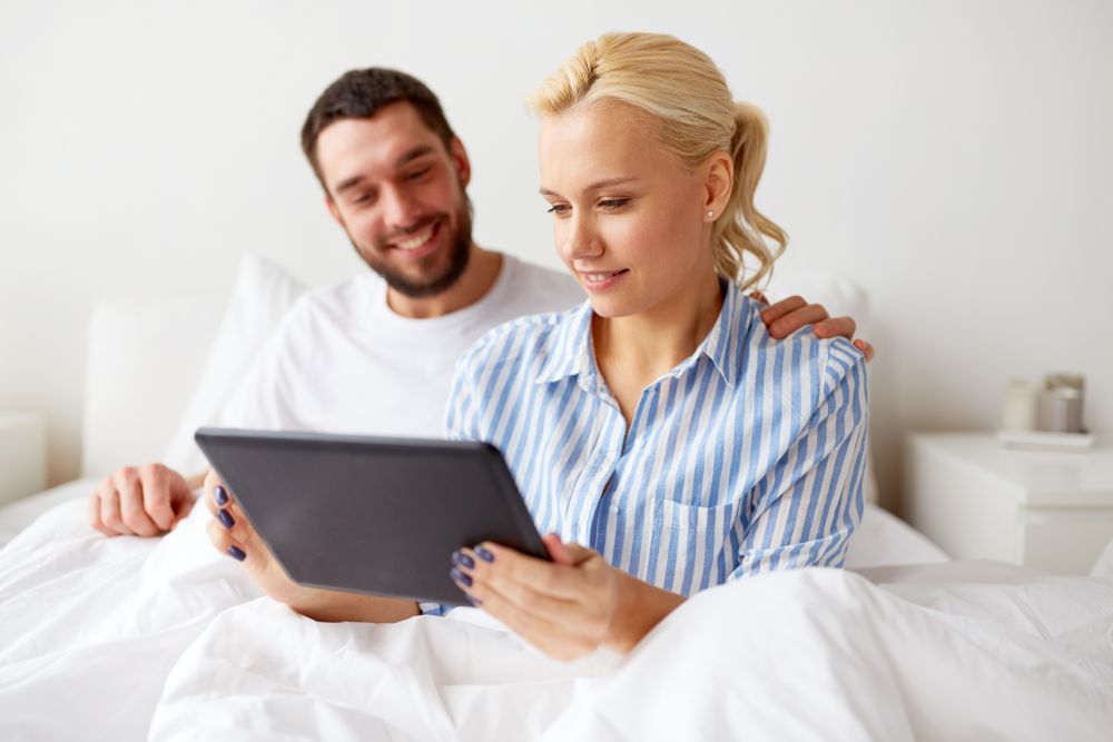 family, technology and people concept - smiling happy couple with tablet pc computer in bed at home bedroom. smiling happy couple with tablet pc in bed at home