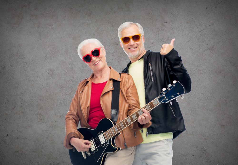 music, age and people concept - happy senior couple in sunglasses with electric guitar showing thumbs up over gray background. happy senior couple with guitar showing thumbs up