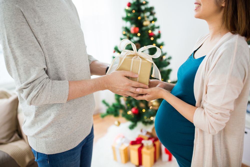 pregnancy, winter holidays and people concept - close up of husband giving christmas present to his pregnant wife at home. husband giving christmas present to pregnant wife