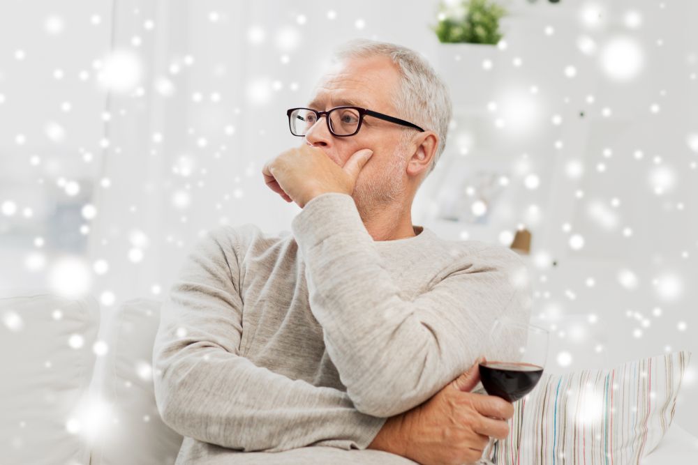 people, alcohol and drinks concept - senior man drinking red wine from glass at home over snow. senior man drinking red wine from glass at home