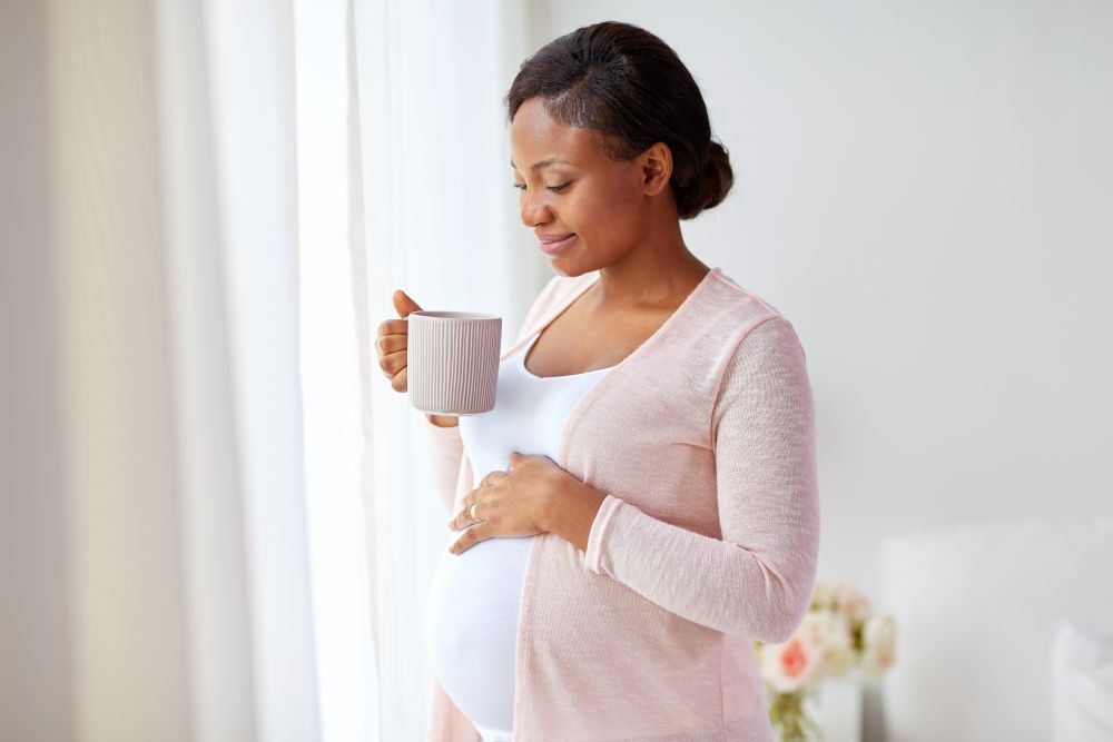 pregnancy, people and expectation concept - happy african american pregnant woman with cup drinking tea at home. happy pregnant woman with cup drinking tea at home