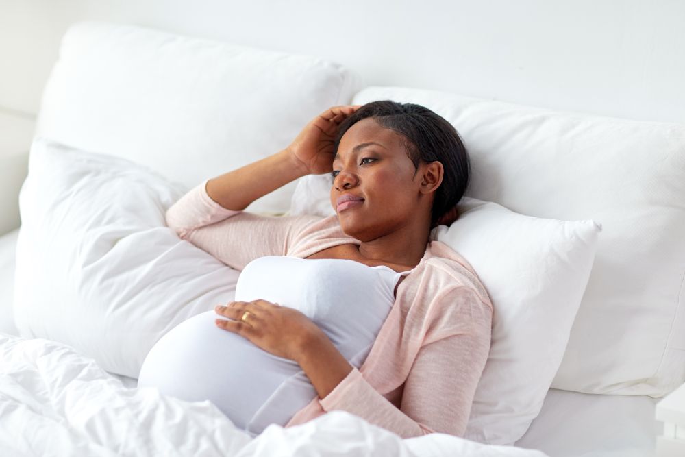 pregnancy, people and health concept - tired pregnant african american woman lying in bed at home. pregnant woman lying in bed at home