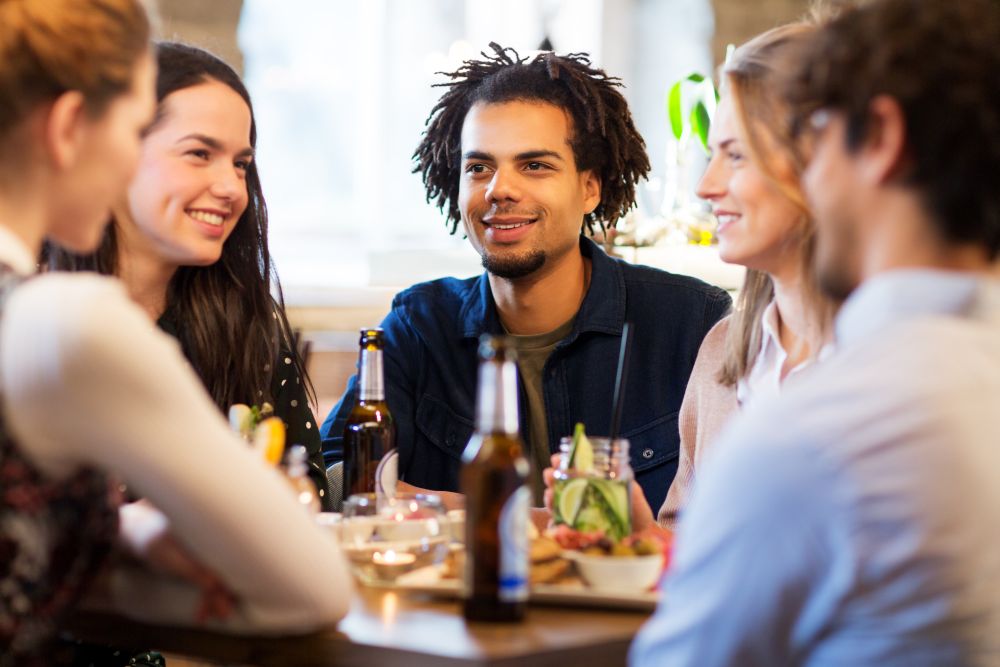 leisure and people concept - happy friends eating and drinking non-alcoholic drinks at bar or restaurant. happy friends eating at bar or restaurant