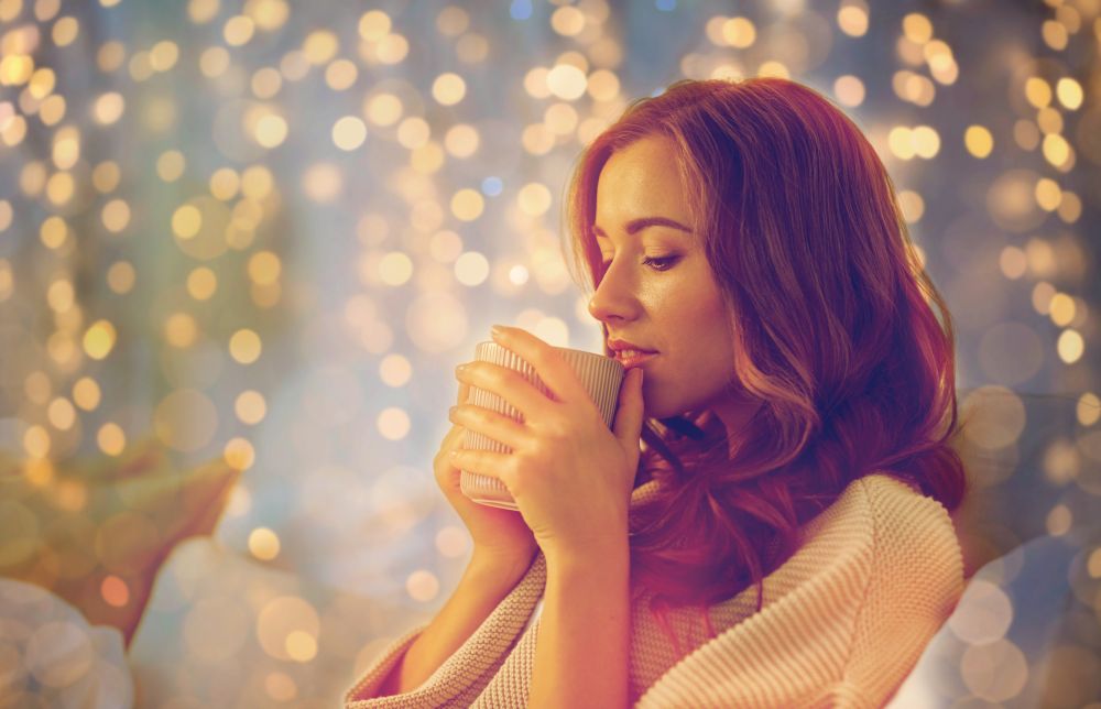 hygge, leisure, christmas and people concept - happy young woman with cup of coffee or tea in bed at home bedroom. happy woman with cup of coffee in bed at home
