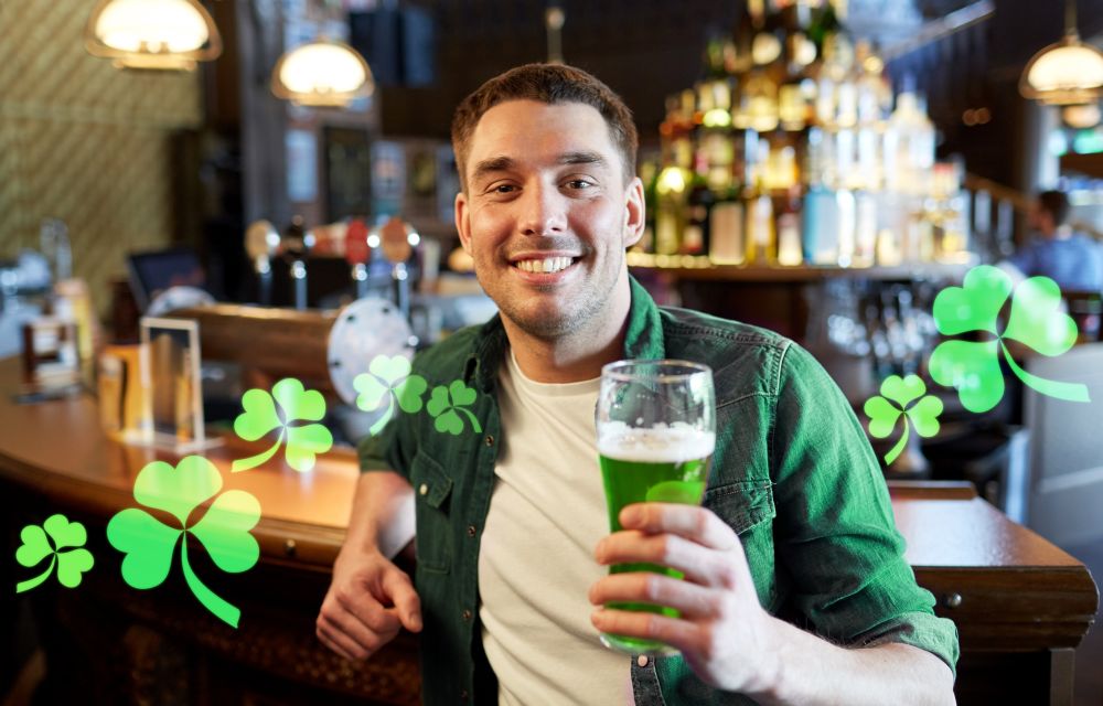 people, leisure and st patricks day concept - happy young man drinking green beer at bar or pub. man drinking green beer at bar or pub