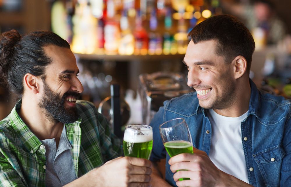 people, leisure and st patricks day concept - happy male friends drinking green beer at bar or pub. male friends drinking green beer at bar or pub