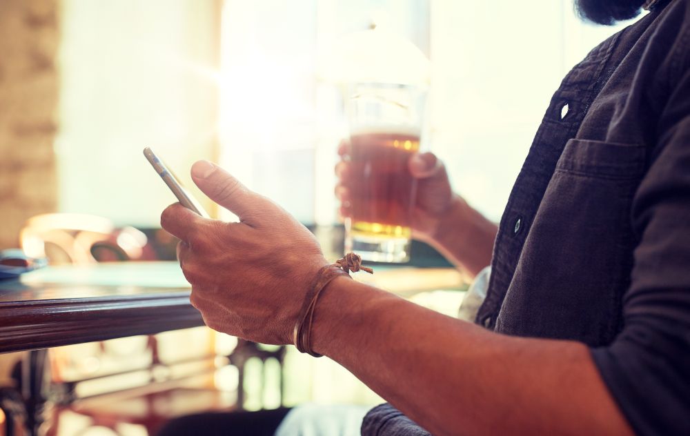 people, leisure and technology concept - close up of man with smartphone drinking beer and reading message at bar or pub. close up of man with smartphone and beer at pub. close up of man with smartphone and beer at pub