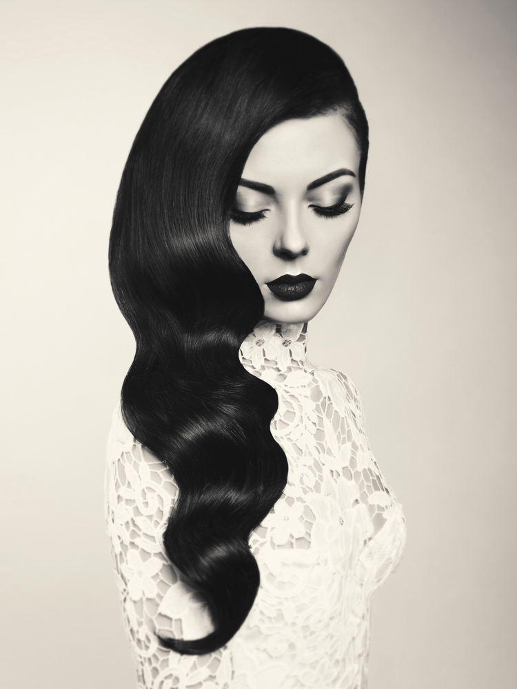 Black and white fashion studio photo of beautiful model girl brunette with long curled hair. Hairstyle Hollywood wave