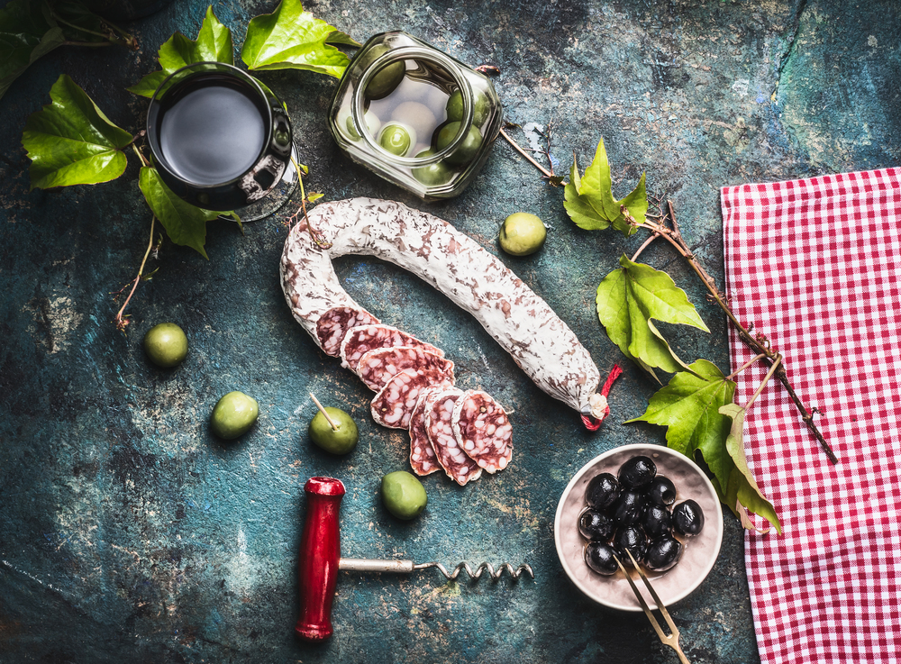 Italian food still life with glass of red wine, olives and sausage  on rustic background, top view