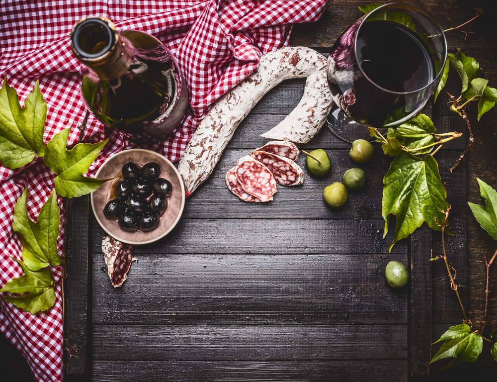 Italian food still life with bottle and a glass of red wine, olives and sausage  on dark rustic background, top view, frame
