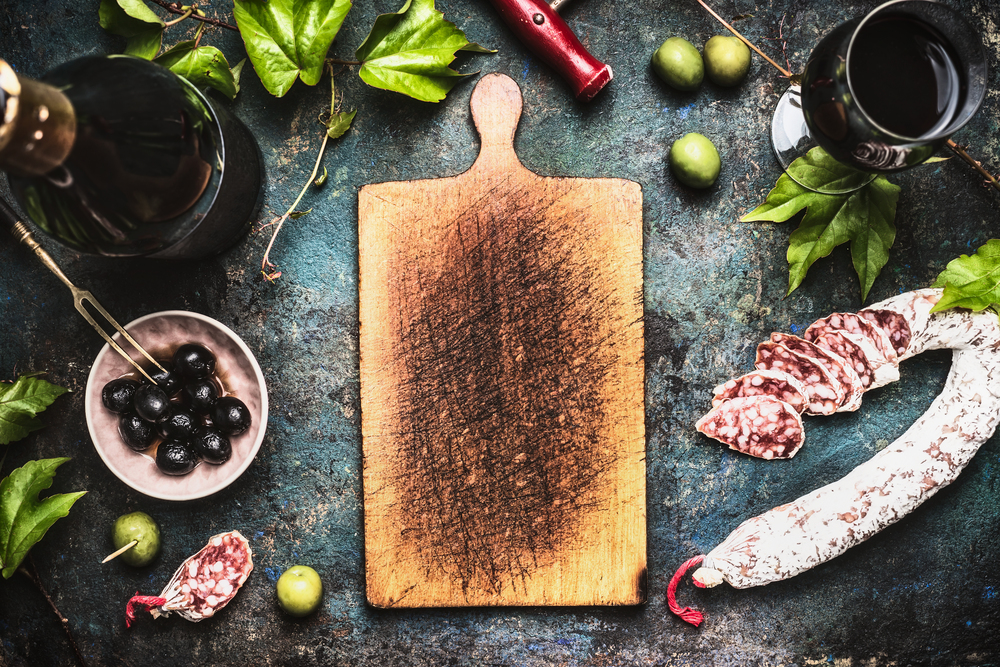Italian food background with wine, olives and  sausage around wooden cutting board, top view