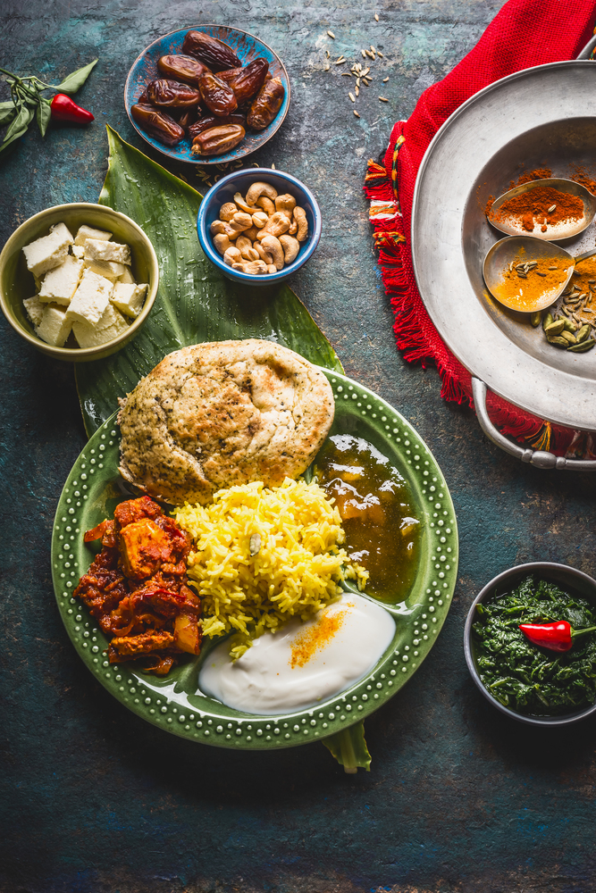 Assorted indian food. Bowls with paneer cheese , curries, rice, naan bread, samosas, chicken,chutney and spices on dark rustic background, top view