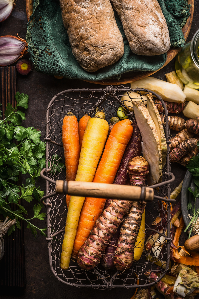Colorful root vegetables in harvest basket on dark wooden kitchen table background, top view. Healthy and clean food and eating  concept.