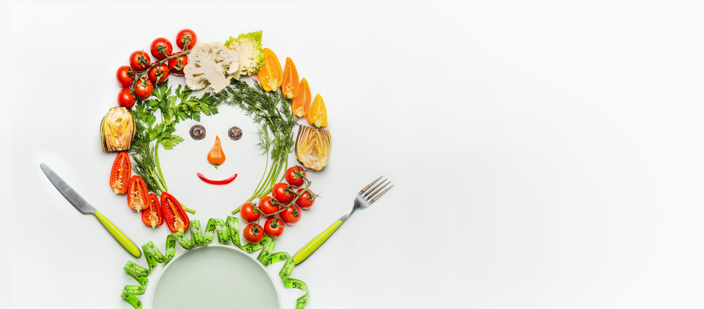 Healthy lifestyle and dieting concept. Friendly Man made of salad vegetables , plate, cutlery and measuring tape on white desk background, top view, place for text. Clean food and vegetarian eating