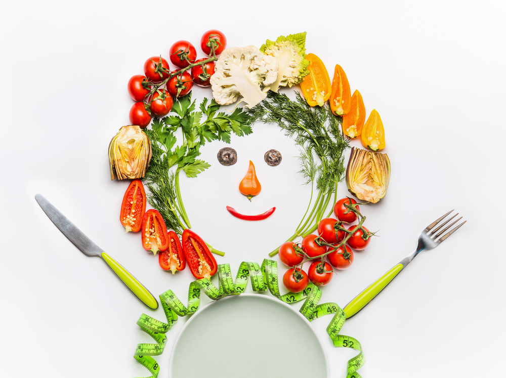 Healthy lifestyle and dieting concept. Friendly Man made of salad vegetables , plate, cutlery and measuring tape on white desk background, top view. Clean food and vegetarian eating