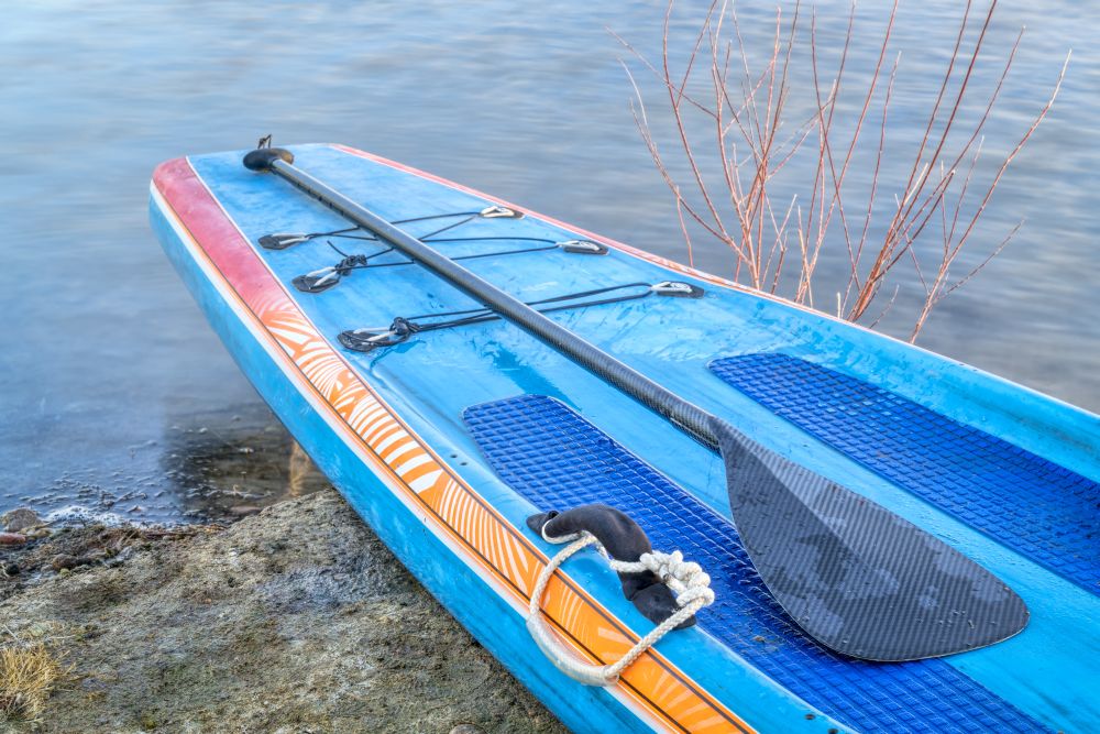 a racing stand up paddleboard with a a paddle on a lake shore