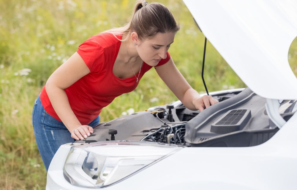 Young woman looking on the motor of broken car in field