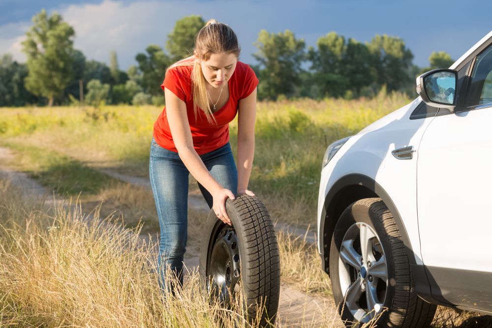 Beautiful woman rolling spare tire to change the flat one