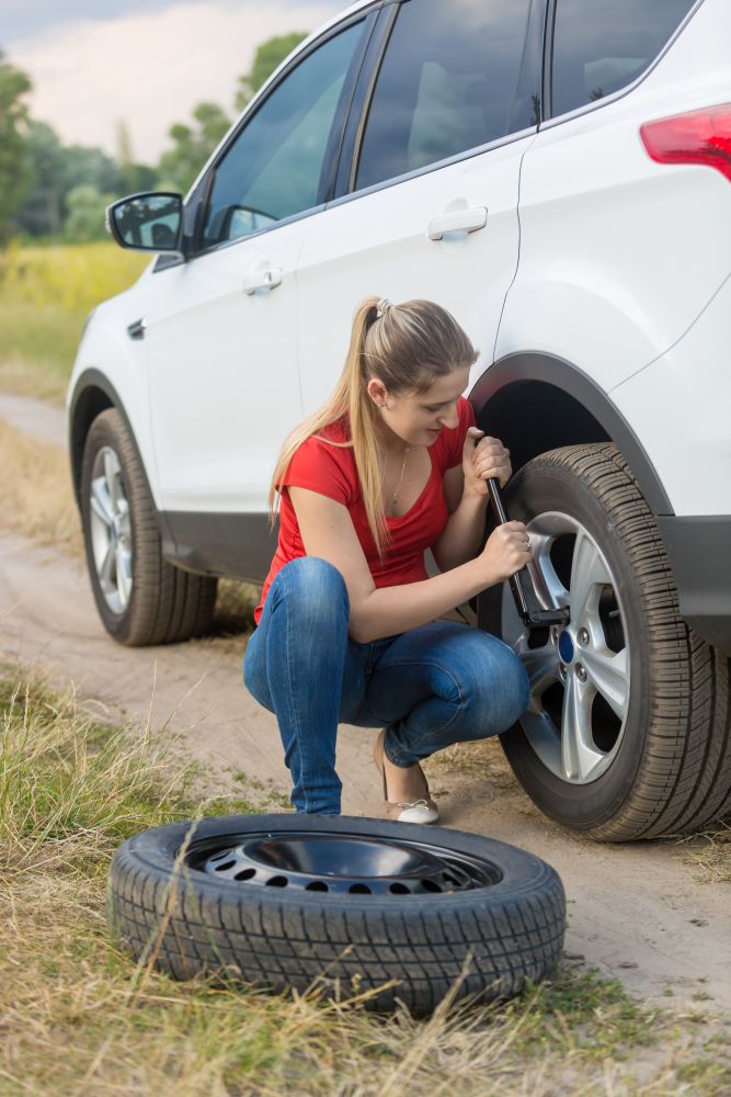 Woman unscrewing nuts on car flat wheel at field
