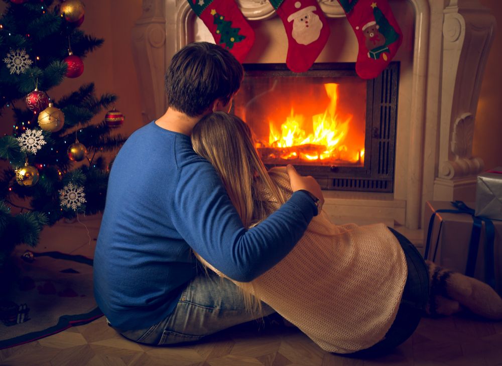 Couple in love sitting on floor and looking at fireplace and decorated Christmas tree