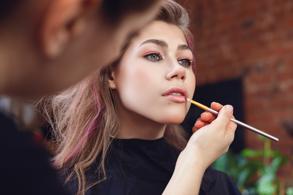 Make-up artist applying lipstick with a brush on model&rsquo;s lips, close up on model&rsquo;s face