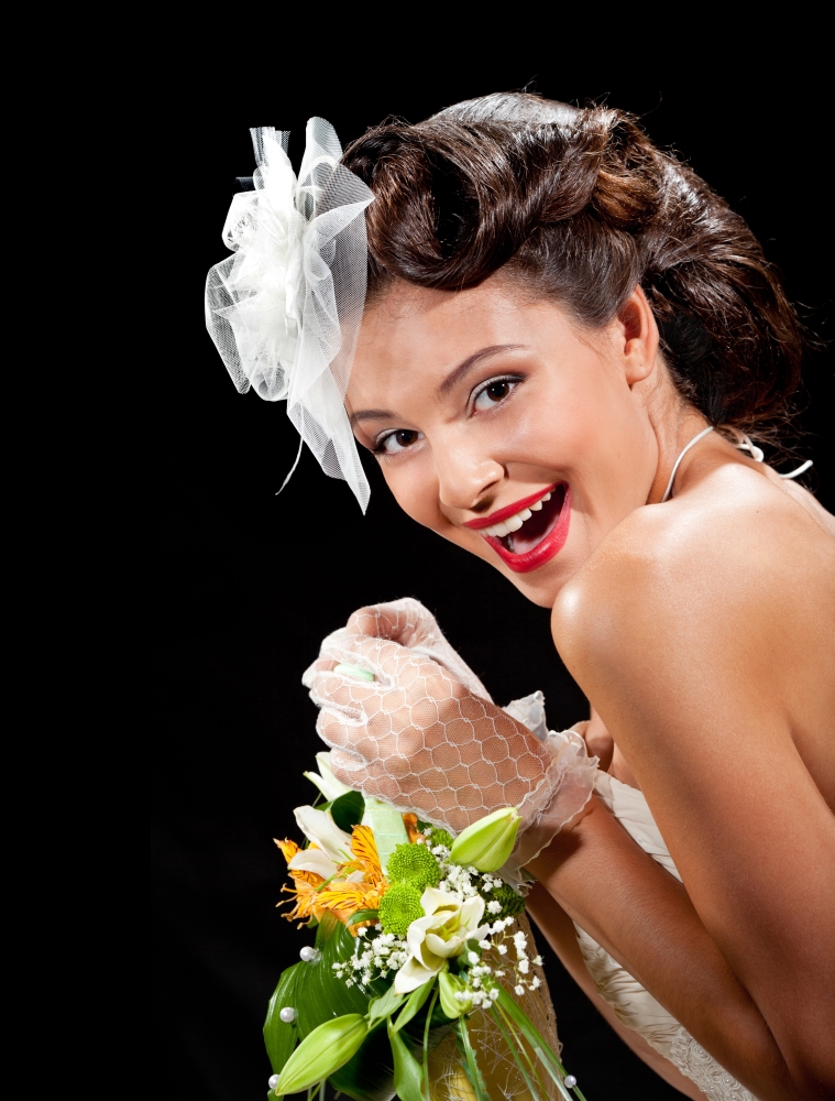 Portrait of Loughing Retro Elegant Bride in Wedding Dress,  White Necklace and Fancy Hat with Bouquet of Orange and Green Flowers at the White Background.