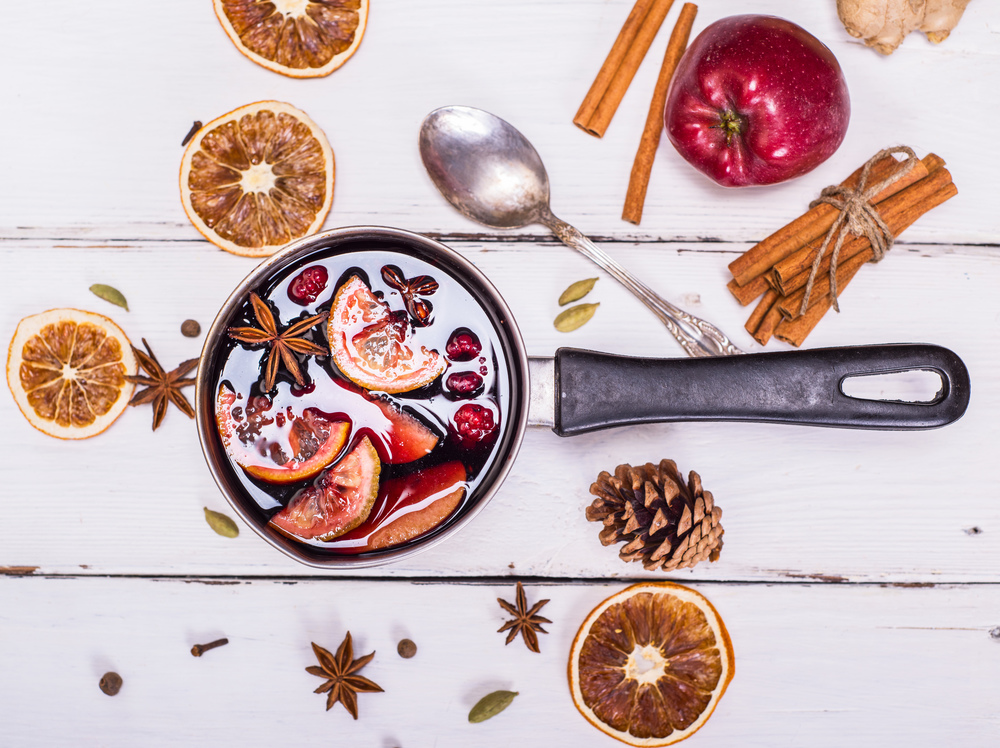 mulled wine with spices and fruits in an aluminum container on a white wooden background, top view