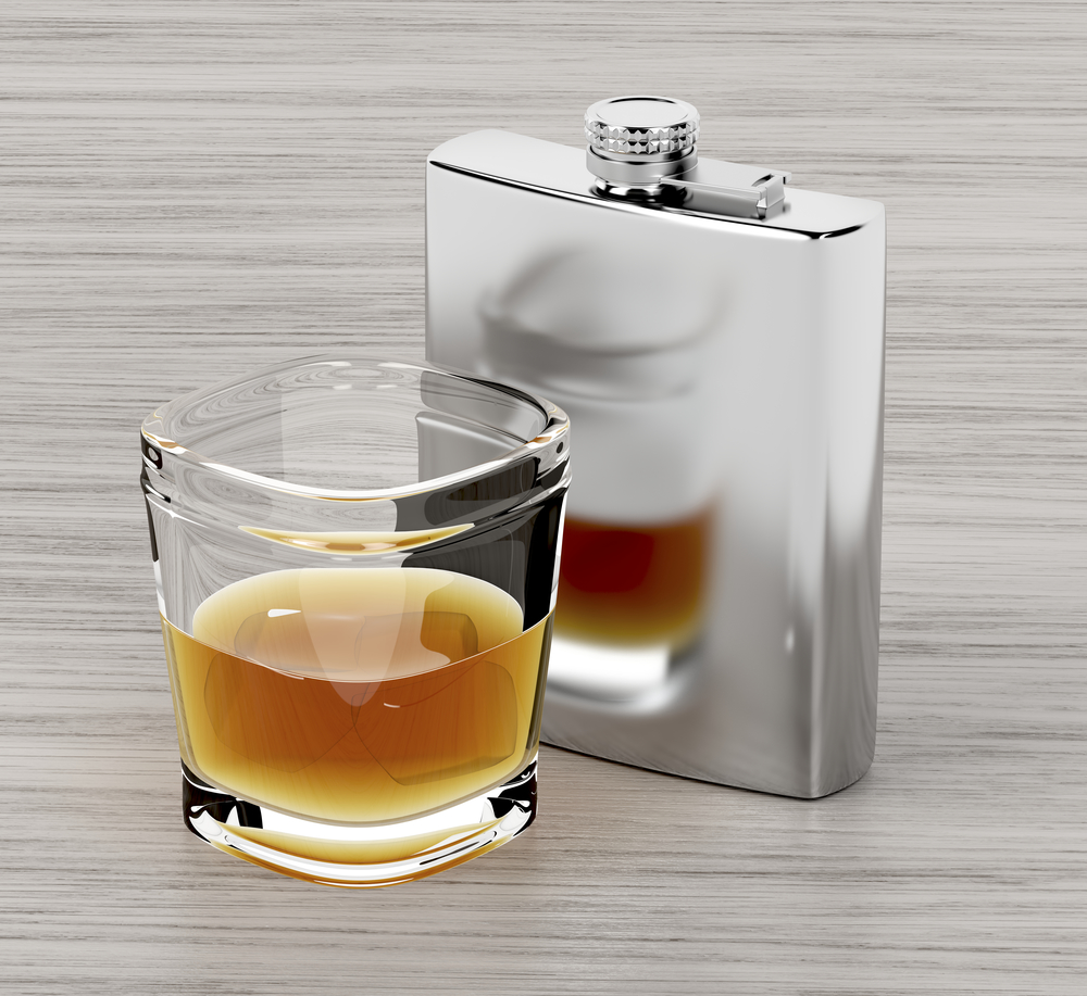 Hip flask and a glass of brandy on wooden table
