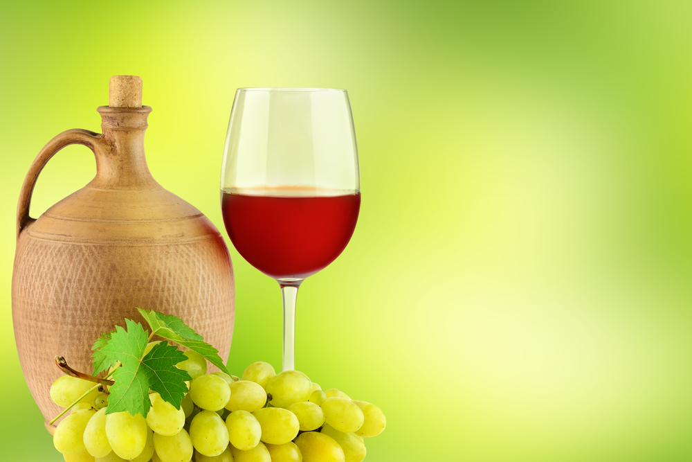 Pitcher with grape wine, glass and bunch grapes on blurred green background