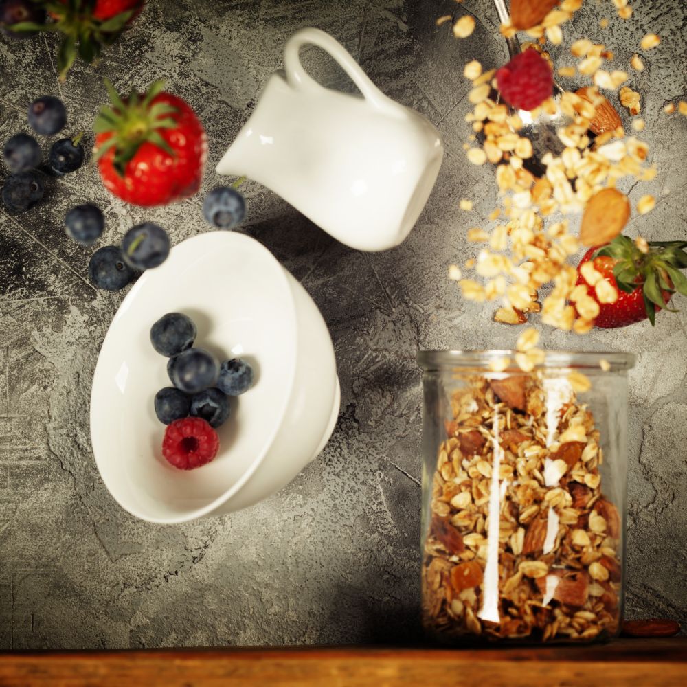 Flying breakfast against grey wall. Granola and berries falling or flying in motion.