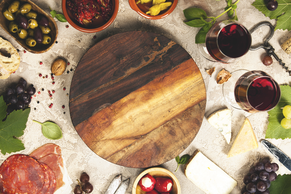 Wine and snack set. Variety of cheese, mediterranean olives, prosciutto,baguette slices, black and green grapes, sun-dried tomatoes, peppers and glasses of red wine over grey marble background, top view, copy space